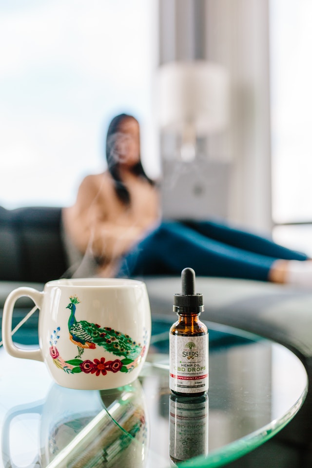 bottle of cbd drops next to cup with hot drink 3259597