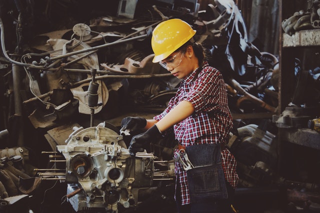 woman wears yellow hard hat holding vehicle part 1108101